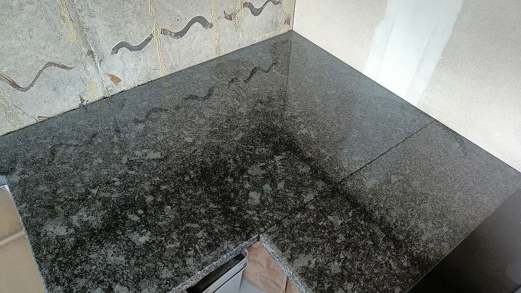 Hörn av en polerad köksbänkskiva i Steel Grey granit med fin spräcklig ådring i ett kök i Staffanstorp.