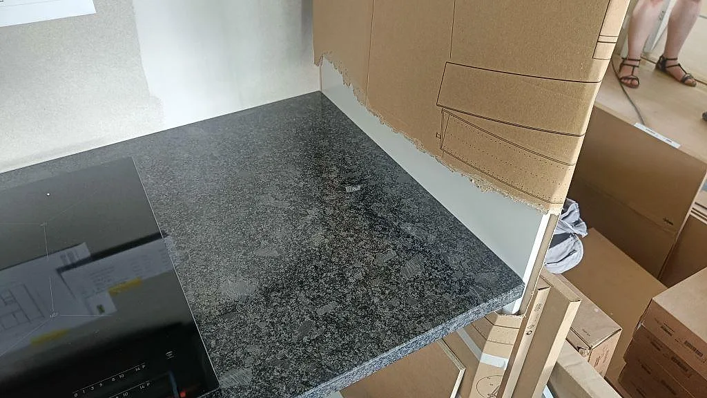 Polerad köksbänkskiva i Steel Grey granit med synlig stenkant intill induktionshällen i ett kök i Staffanstorp.
