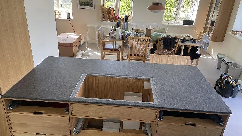 Köksbänkskiva på köksö i matt Steel Grey granit med förberedd öppning i stenen i ett kök i Stege under montering.