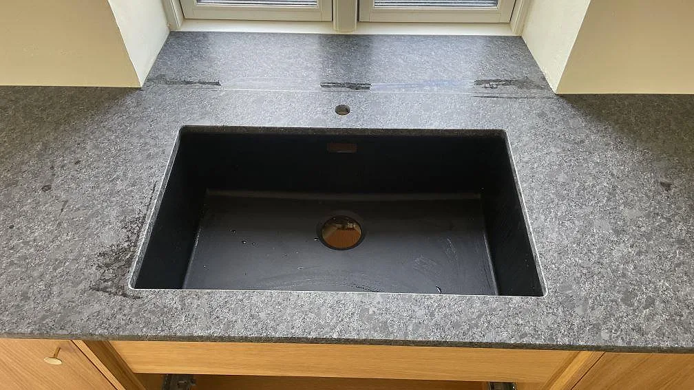 Närbild på svart diskho i matt Steel Grey granit, monterad i väggbänken under fönstret i köket i Stege.