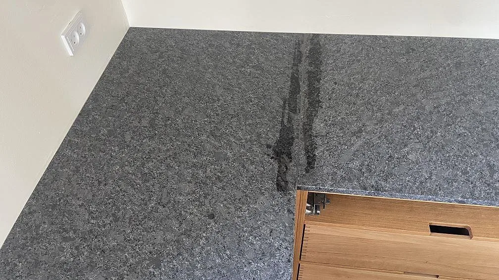 Närbild på matt Steel Grey granit och mörk övergång på köksbänk längs väggen i Stege under montering.