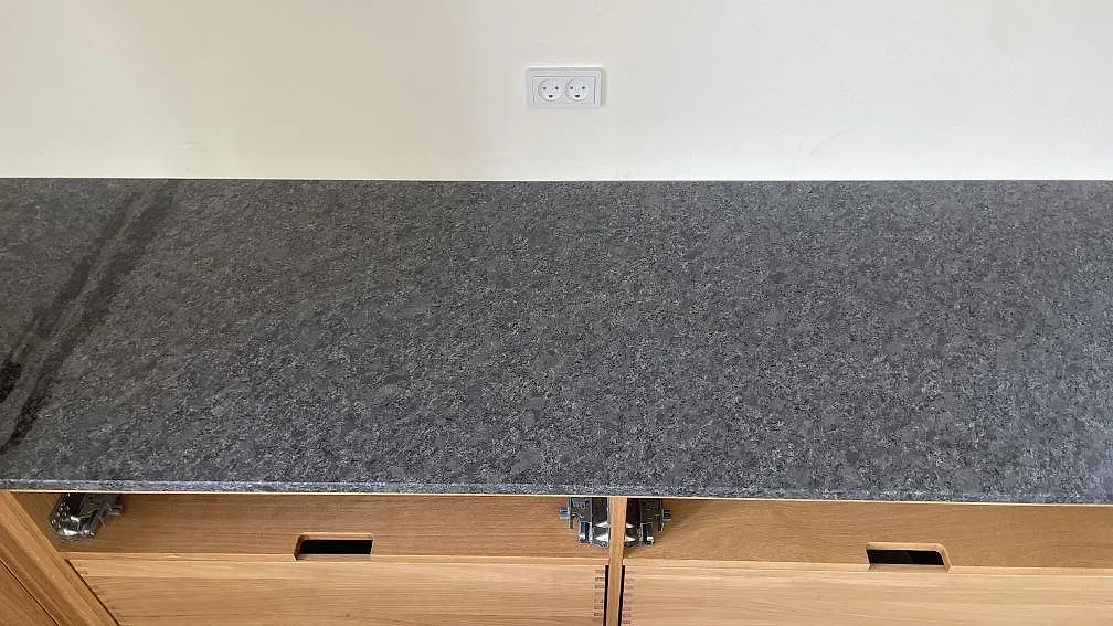 Rak väggbänk i matt Steel Grey granit med synlig framkant och trästommar i köket i Stege.
