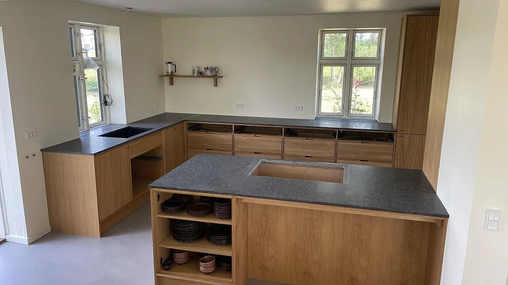 Köksbänkskiva i matt Steel Grey granit med köksö, väggbänk och svart diskho i ett kök i Stege under montering.