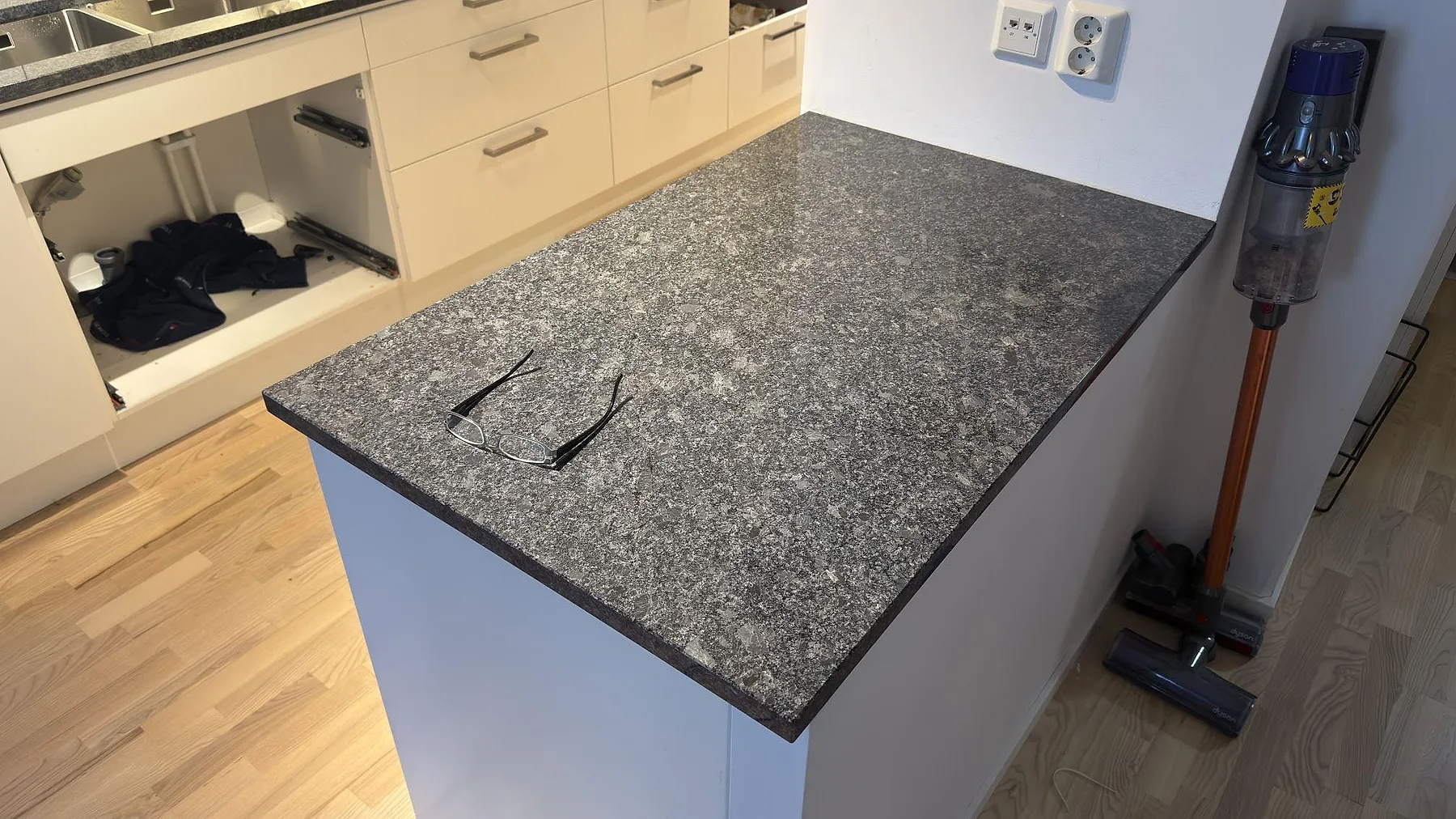 Köksö i polerat Steel Grey-granit med tydlig kristallin gråsvart ådring, fotad under montering i ett kök i Stockholm.