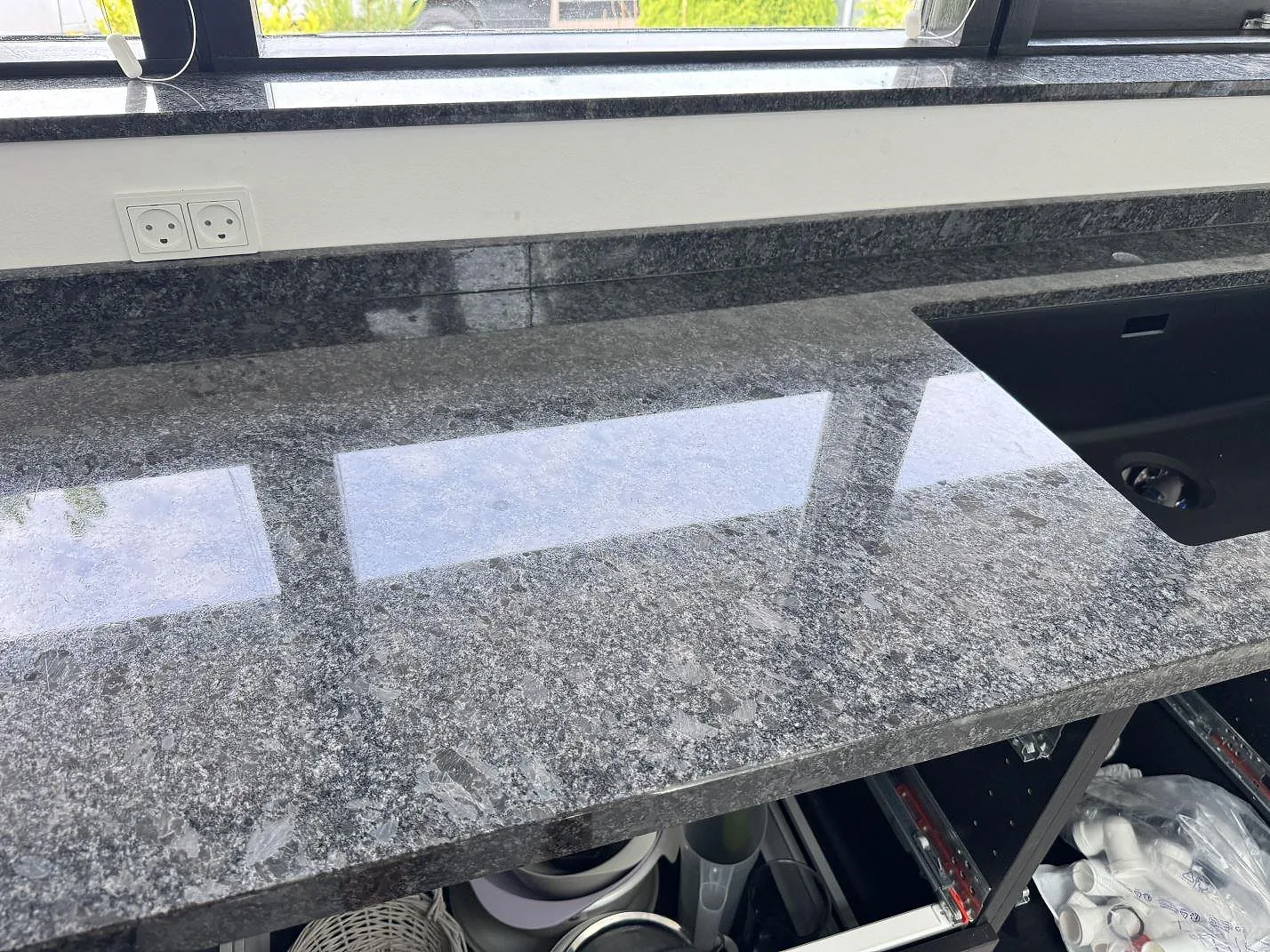 Blankpolerad Steel Grey granitbänkskiva med mörk diskho, stänkkant och fönsterbänk i köket i Tølløse.