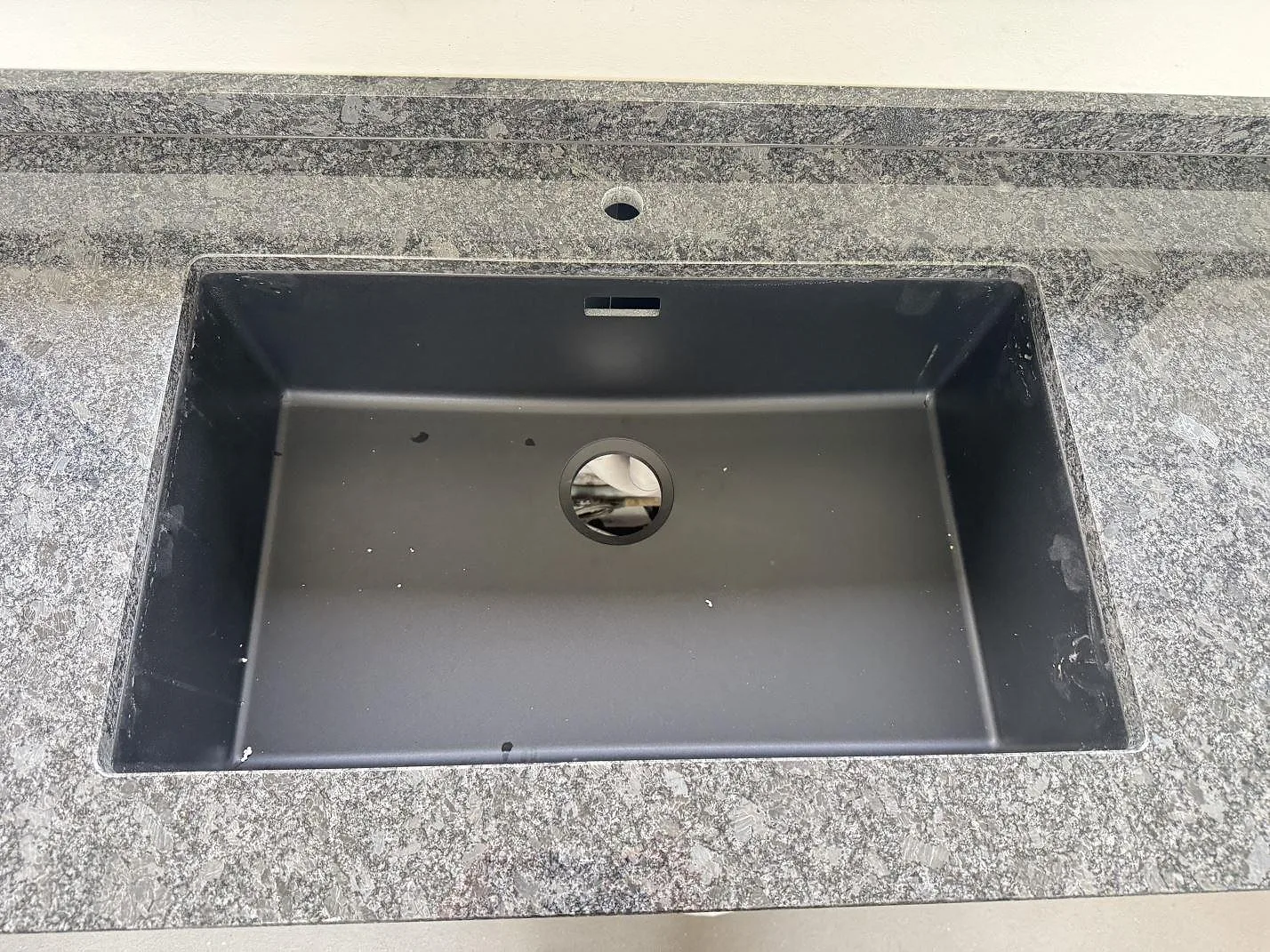 Närbild på mörk diskho monterad under en polerad Steel Grey granitbänkskiva med stänkkant i Tølløse.