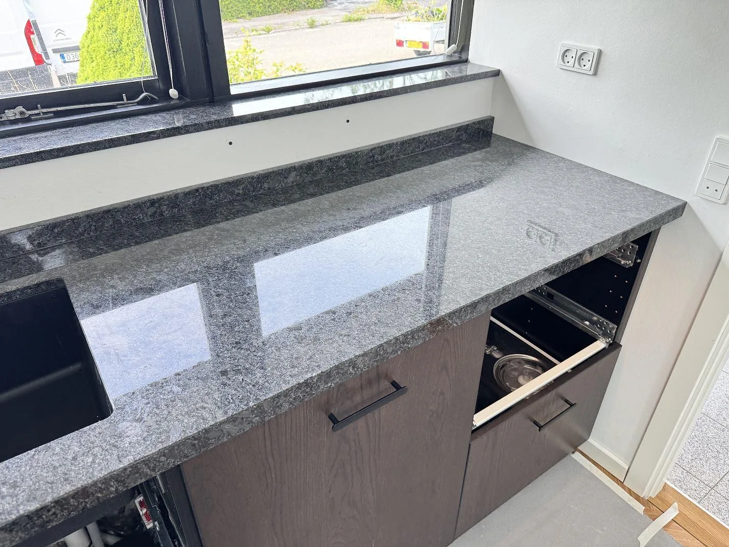 Polerad Steel Grey granitbänkskiva med mörk diskho, låg stänkkant och fönsterbänk under montering i Tølløse.