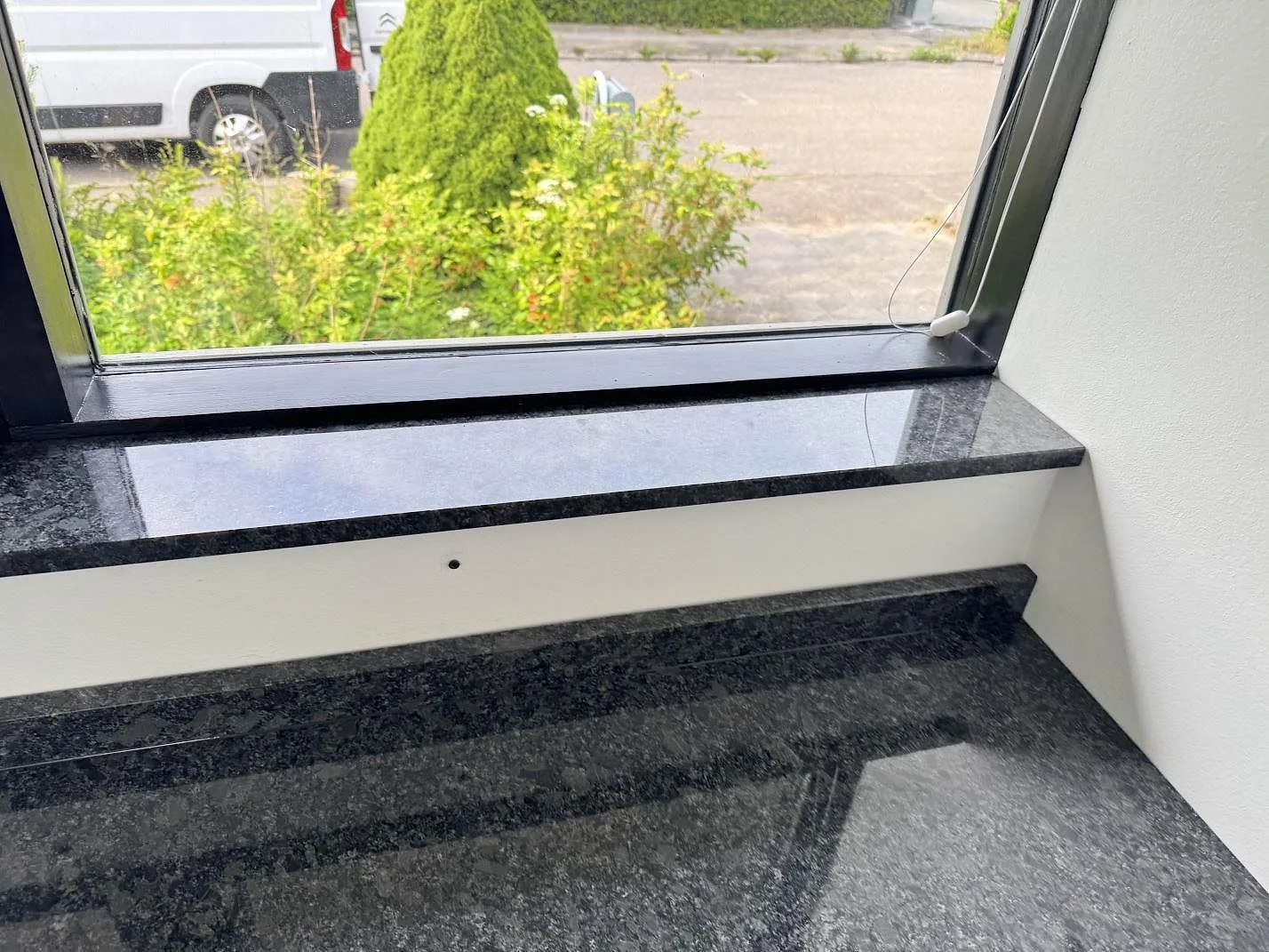 Fönsterbänk i polerad Steel Grey granit ovanför köksbänkskiva med stänkkant under montering i Tølløse.