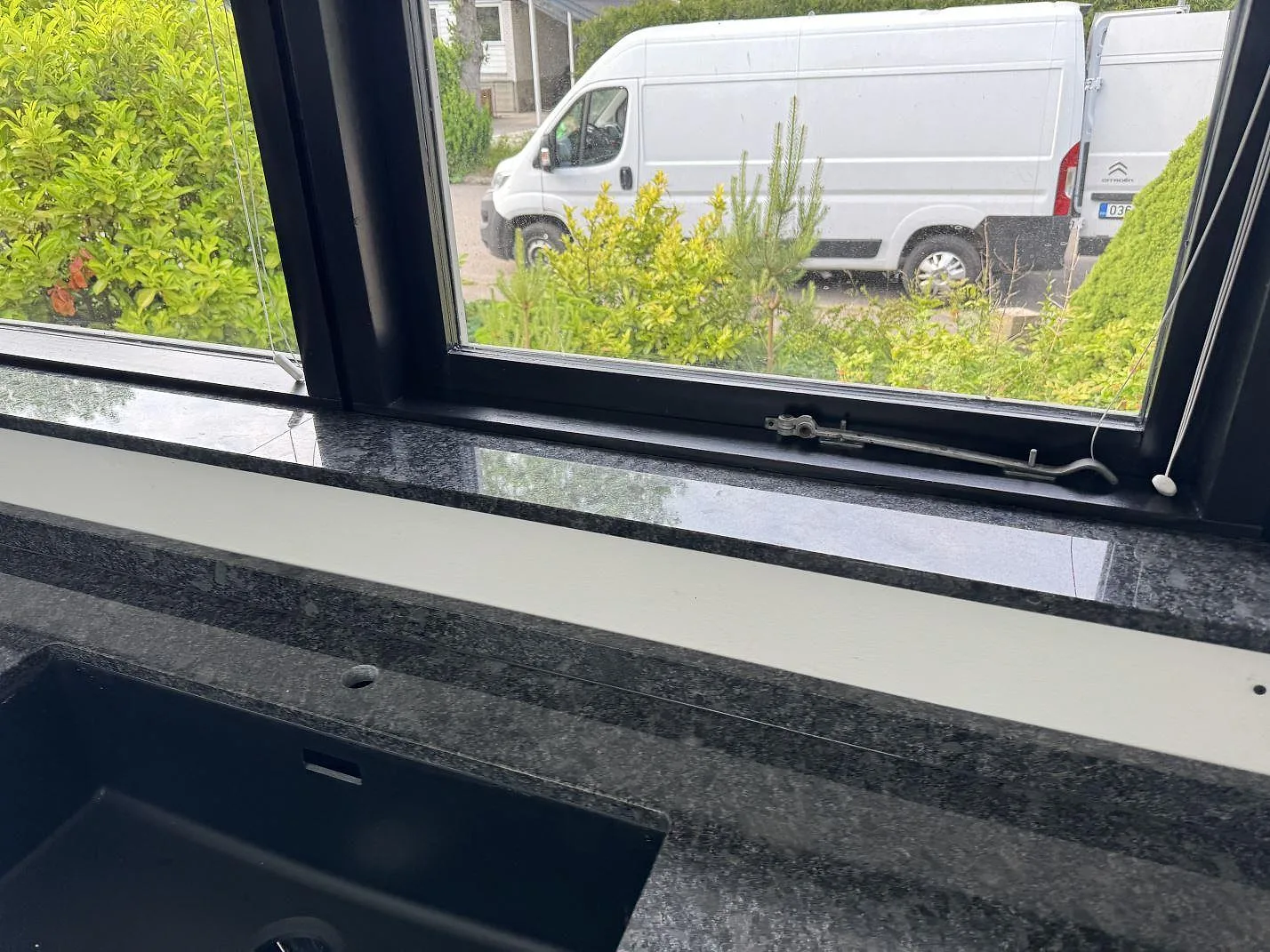 Polerad fönsterbänk och bänkskiva i Steel Grey granit vid köksfönster och mörk diskho i Tølløse.