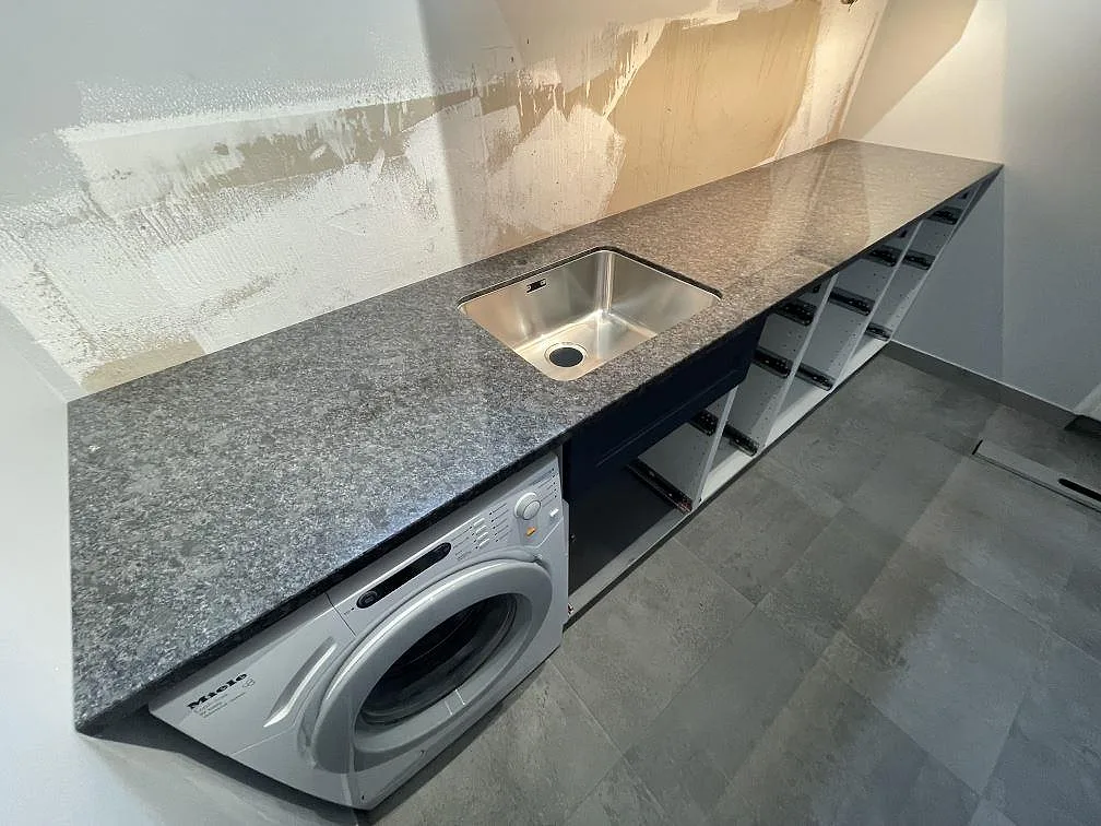 Närbild av polerad Steel Grey granitbänkskiva med diskho och grått stenlikt golv under montering i Tumba.