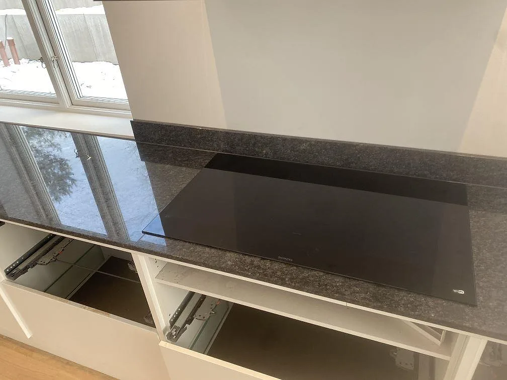Bänkskiva i polerad Steel Grey granit med svart häll och låg stänkkant i ett kök i Uddevalla.