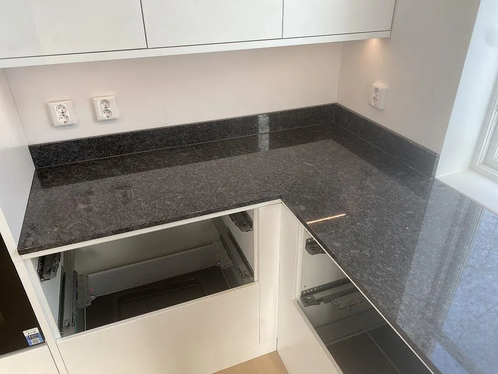 Hörnparti med bänkskiva och uppvikt stänkkant i polerad Steel Grey granit i Uddevalla.