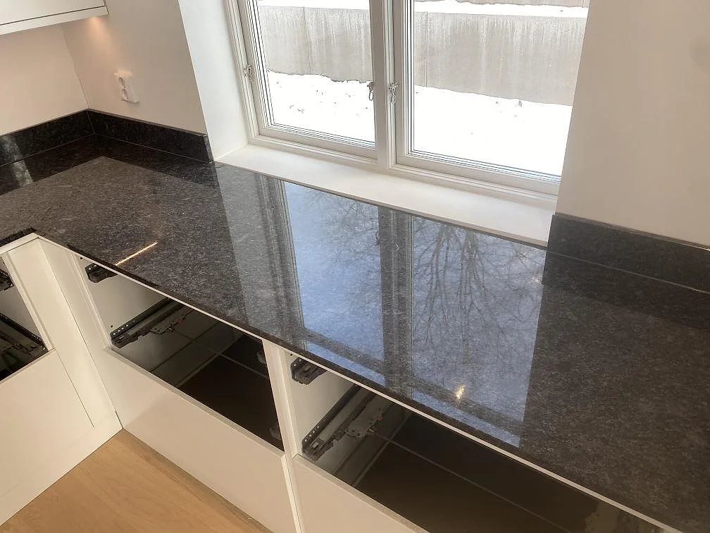Blank bänkskiva i polerad Steel Grey granit framför stora fönster och vita stommar i Uddevalla.
