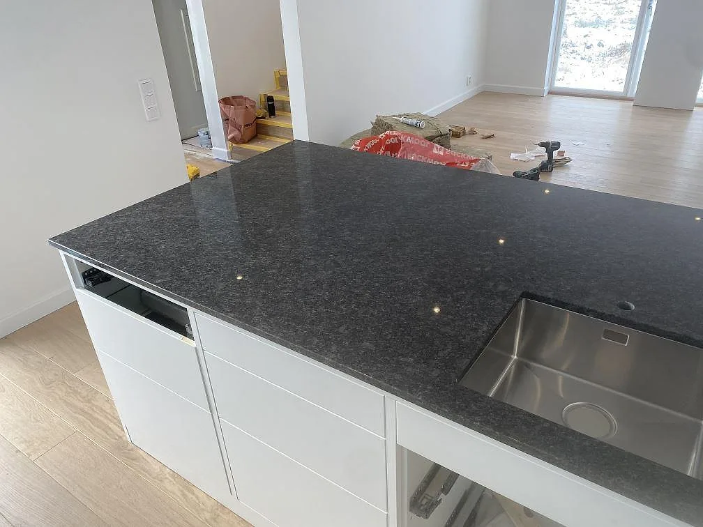 Närbild på stor köksö i polerad Steel Grey granit med monterad rostfri diskho i Uddevalla.