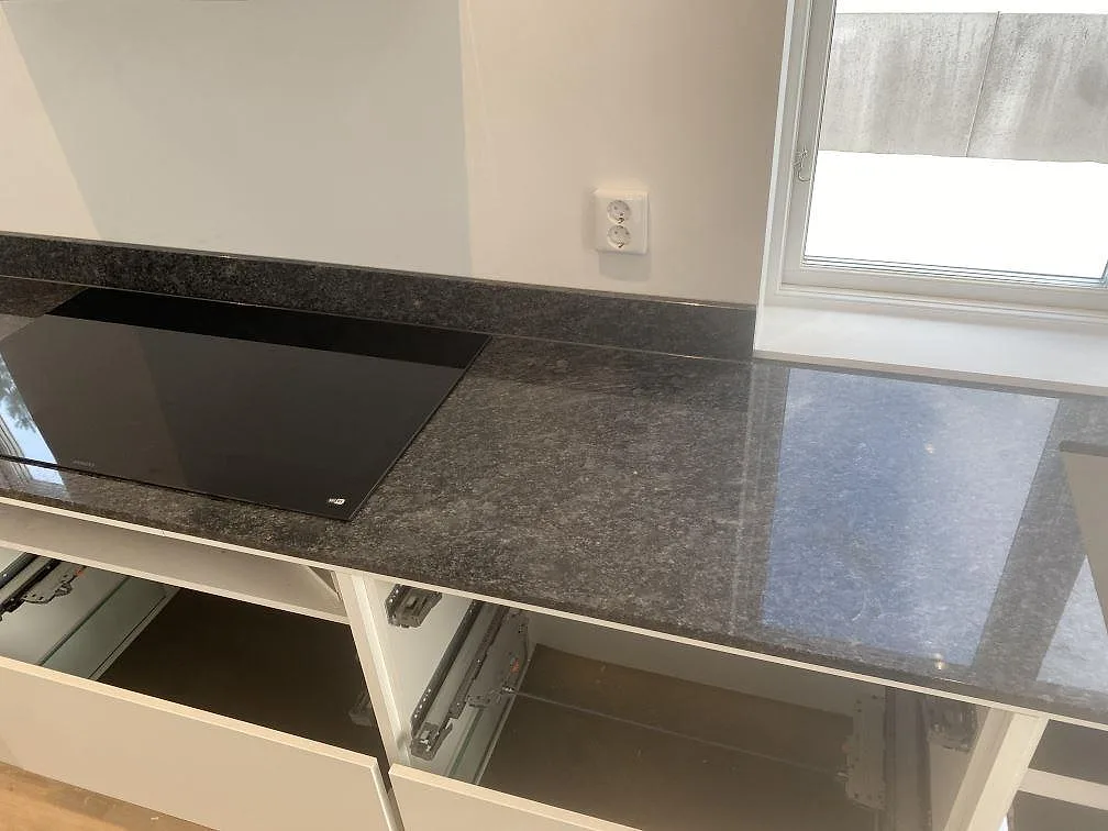 Detalj av polerad Steel Grey granit vid häll, fönster och låg stänkkant i köket i Uddevalla.