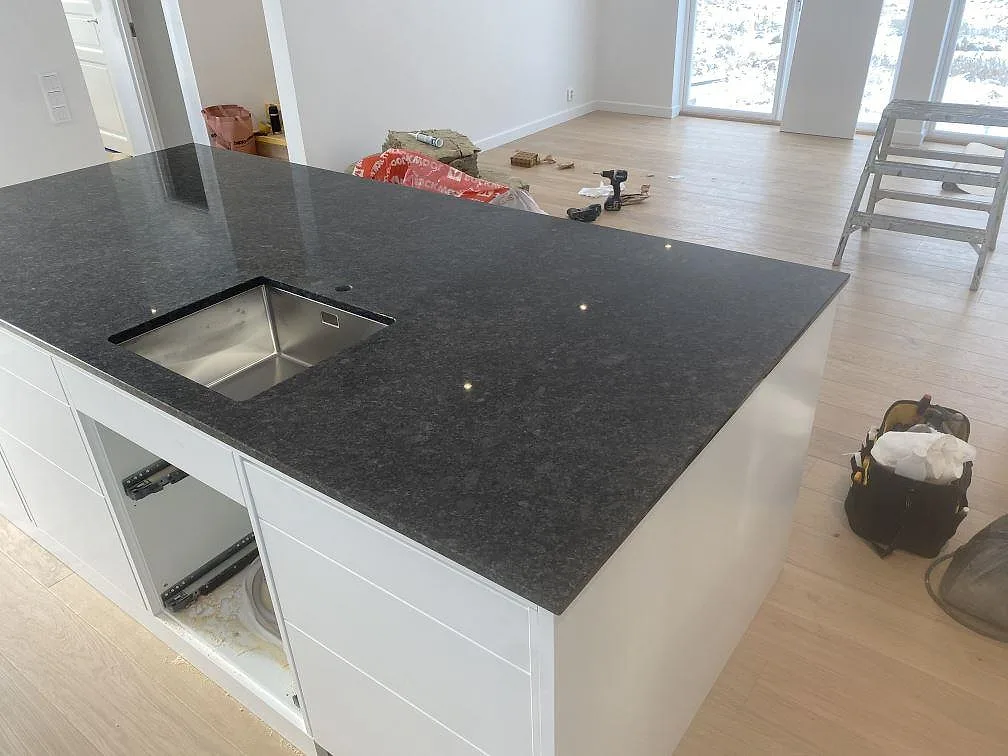 Köksö i polerad Steel Grey granit med rostfri diskho och vit köksinredning i Uddevalla.