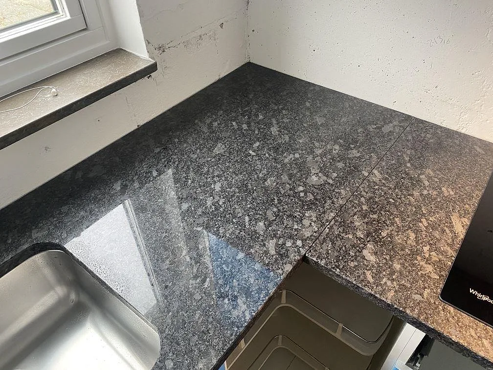 Hörn av polerad Steel Grey granitbänkskiva vid fönstret med rostfri diskho i ett kök i Västra Frölunda.