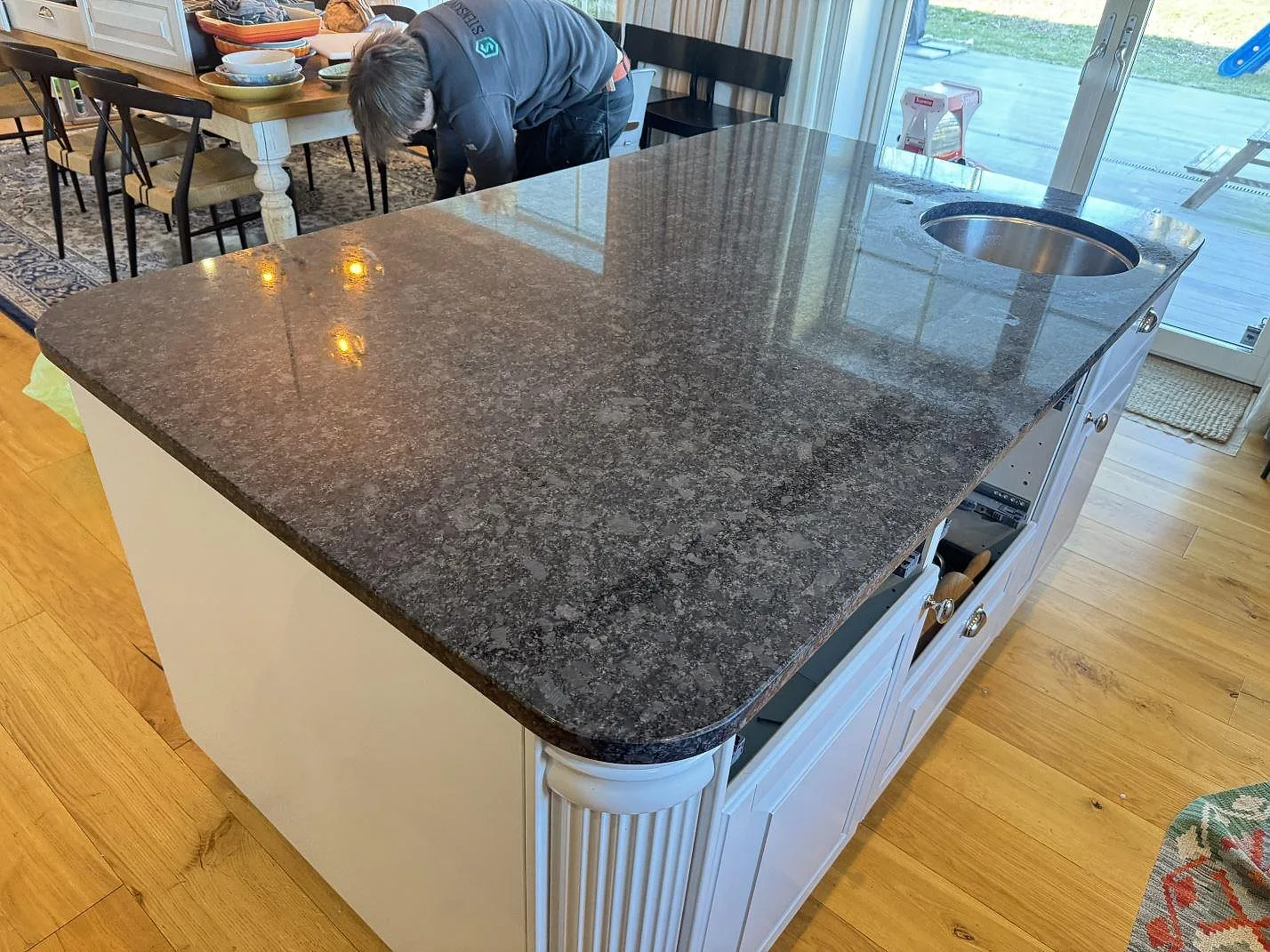 Monteringsbild av köksö i polerad Steel Grey granit i Växjö, med stor arbetsyta, rund diskho och vit köksinredning.