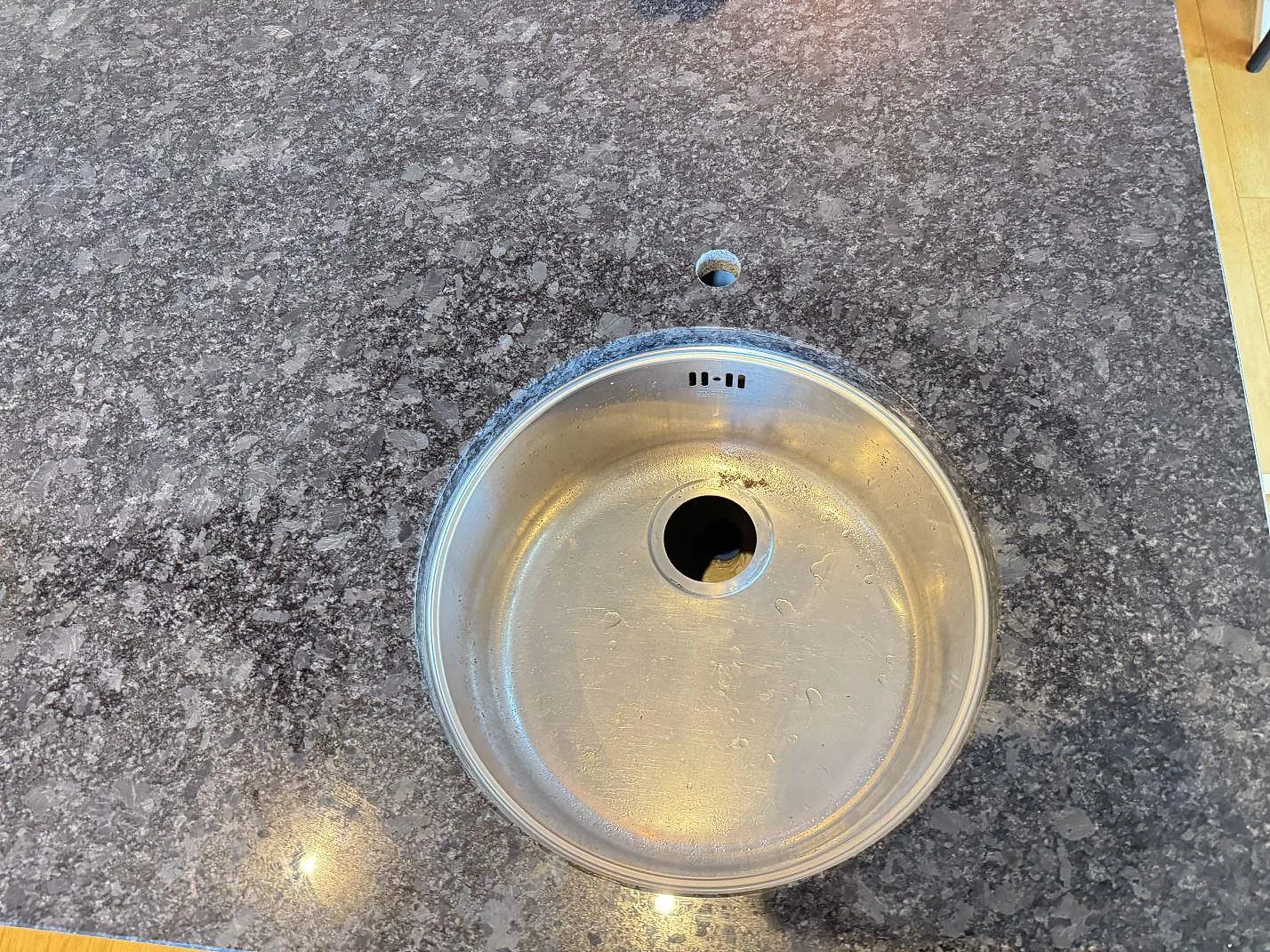 Närbild på rund diskho i en polerad Steel Grey granitskiva i Växjö, med stenens mörkgrå kristallmönster runt öppningen.