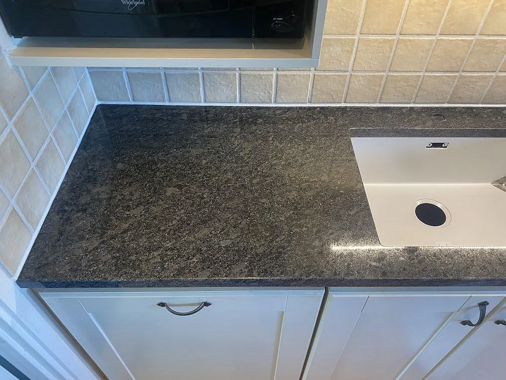 Polerad Steel Grey granitbänkskiva med underlimmad vit diskho under en mikrovågsugn i ett kök i Vejbystrand.