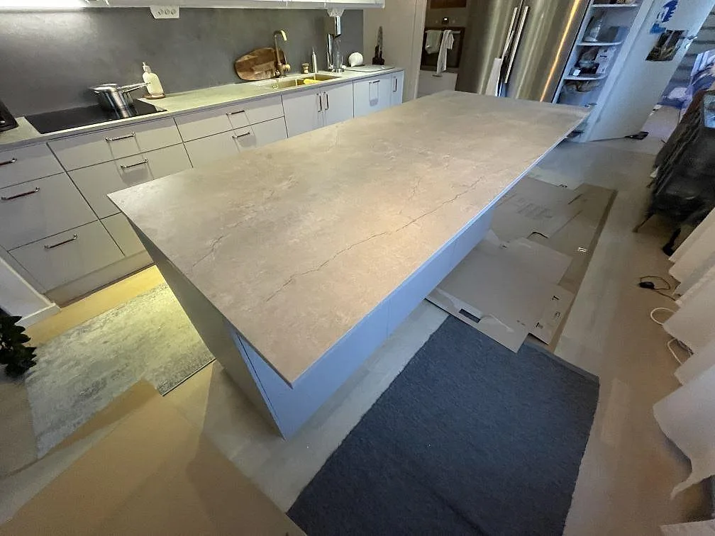 Stor köksö i beige Dekton Soke keramik, matt yta, som frihängande mittpunkt i ett kök i Stockholm med diskho och häll på den bakre bänkraden.