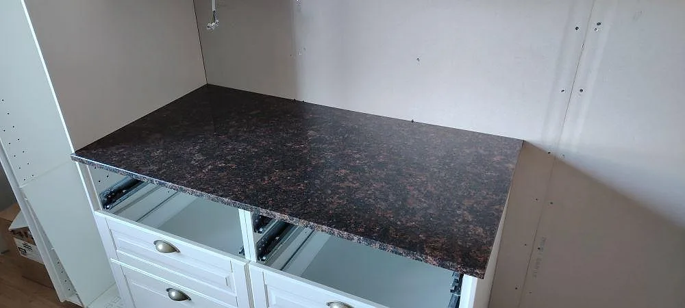 Polerad Tan Brown-granit som rak köksbänkskiva på vita köksstommar, med öppna lådor under montering i Björbo.