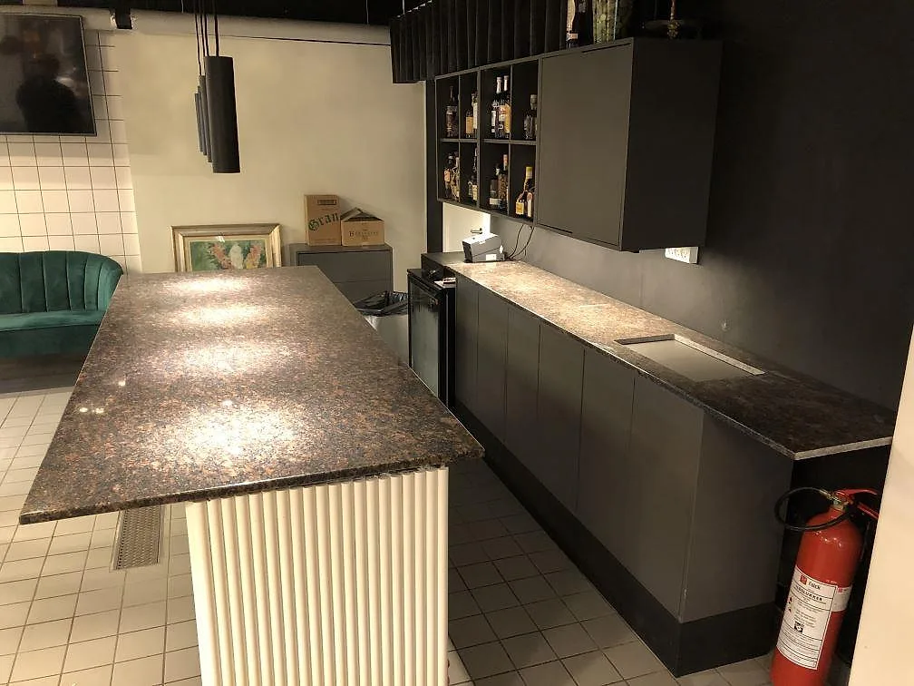 Köksbänkskiva i polerad Tan Brown granit med frihängande bardel på vit sockel, mörka köksstommar och bruna, svarta och rödbruna toner i ett kök i Hellerup.