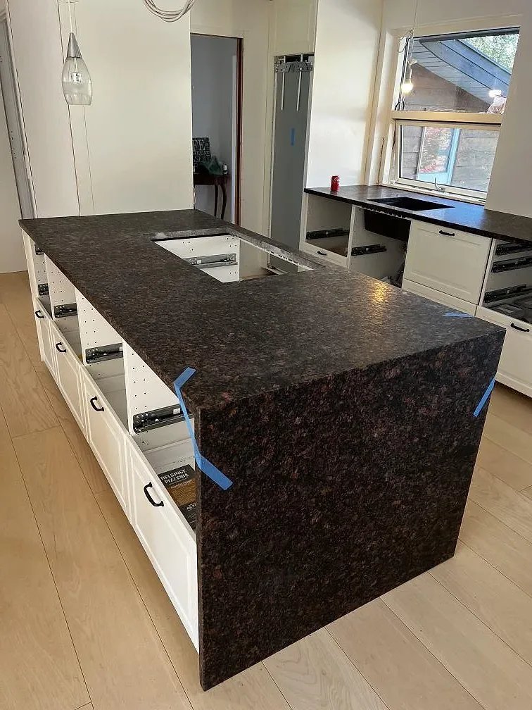 Stor köksö i matt Tan Brown granit med urtag för häll, vattenfallssida och bänkskiva med diskhoöppning i Helsinge.