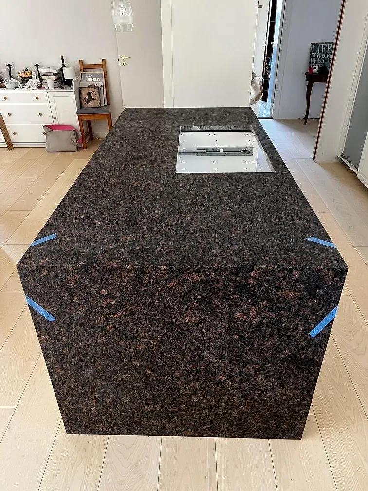 Frontal vy av köksö i matt Tan Brown granit med mörk brunröd stenbild, vattenfallssida och hällurtag i Helsinge.