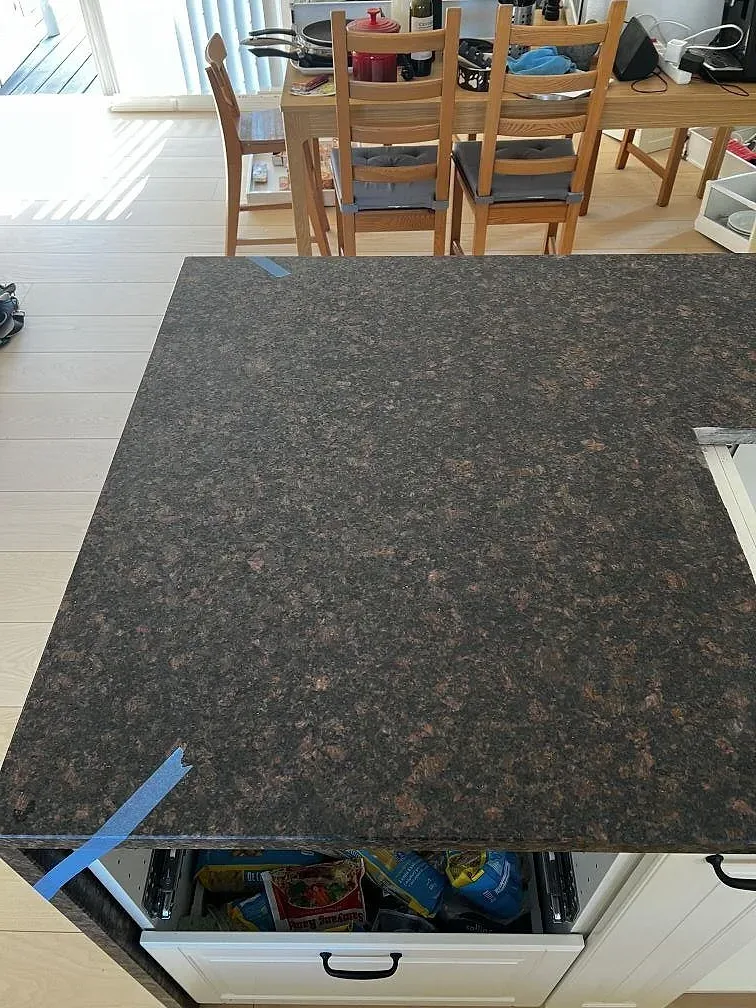 Närbild av matt Tan Brown granit på installerad köksö med brunröda kristaller och öppna vita köksstommar i Helsinge.