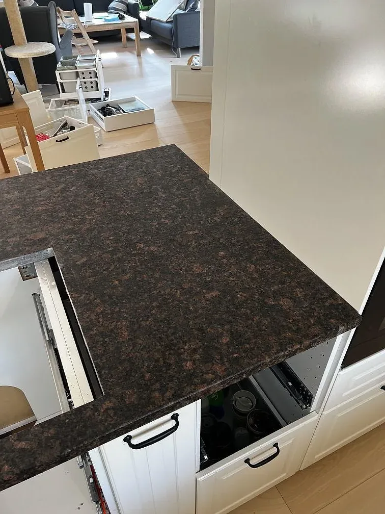 Ytdetalj av matt Tan Brown granit med mörk spräcklig struktur, rak kant och vita köksstommar i Helsinge.