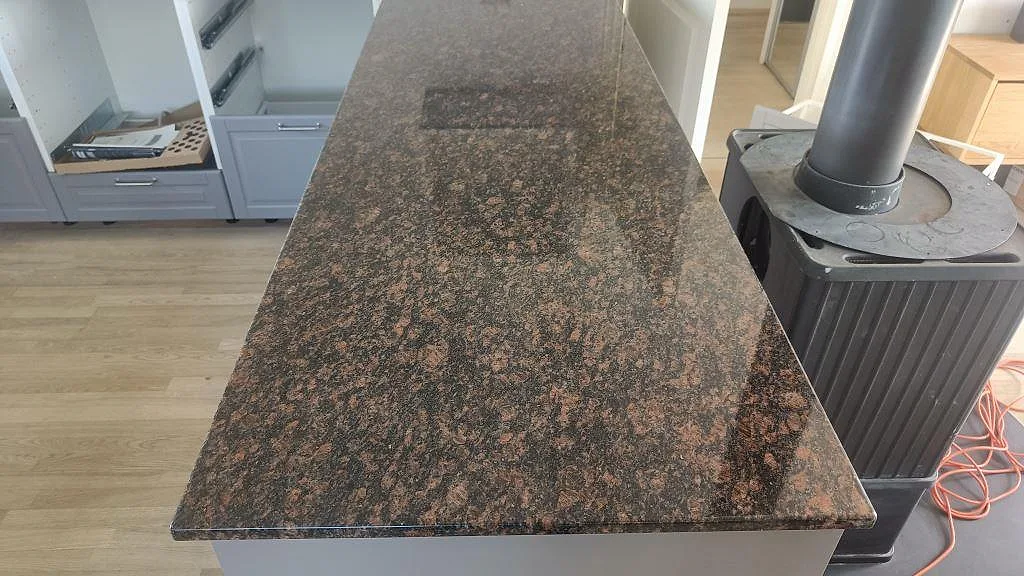 Närbild av polerad Tan Brown granit på kökshalvö med braskamin intill i ett kök i Kastrup.