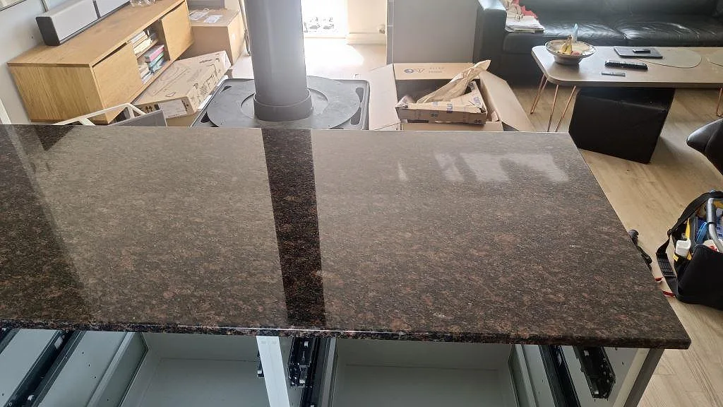 Topvy av polerad Tan Brown granit på kökshalvö mot öppen vardagsdel under montering i Kastrup.