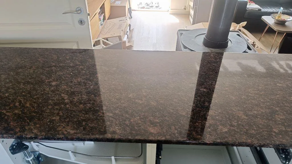 Blank polerad Tan Brown granit på halvö med speglingar från fönster och braskamin i bakgrunden i Kastrup.