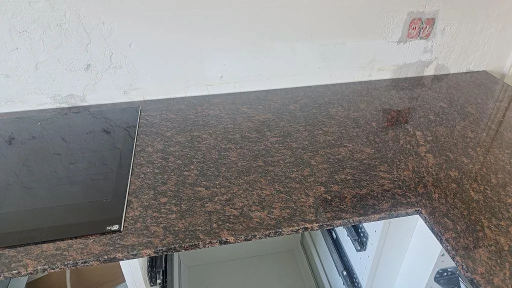 Köksbänkskiva i polerad Tan Brown granit med svart häll och öppna köksstommar under montering i Kastrup.