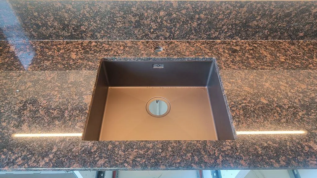 Närbild på underlimmad diskho i polerad Tan Brown granit med brun ådring och LED-ljus under bänkskivan i Malmö.