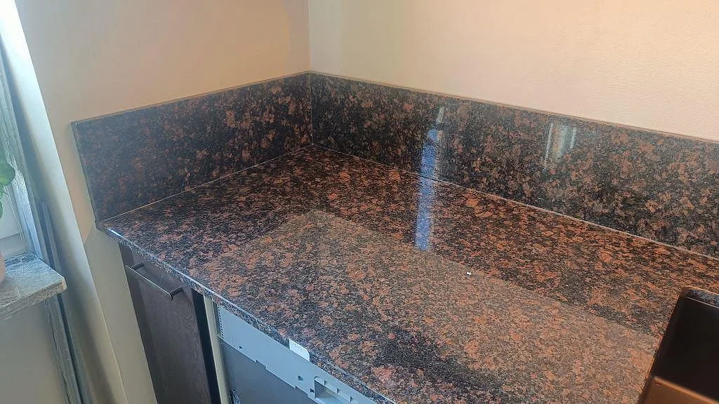 Hörnparti av köksbänkskiva i polerad Tan Brown granit med hög stänkkant och vit köksstomme i Malmö.