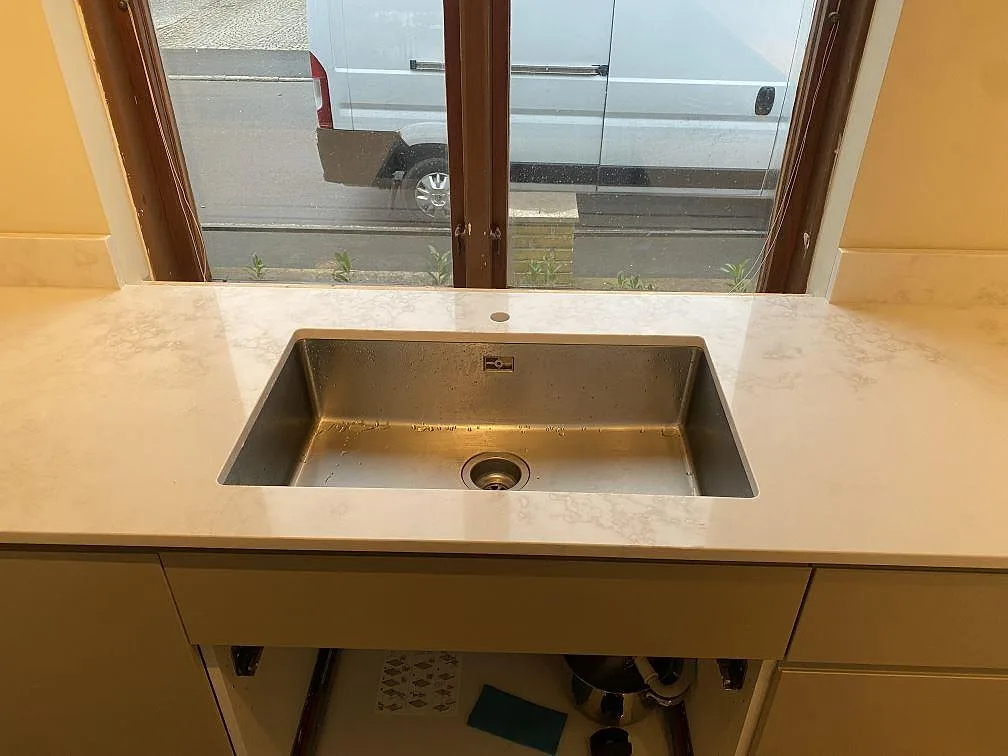 Polerad köksbänkskiva i Technistone Altamonte, komposit, med underlimmad rostfri diskho framför fönster i Landskrona.