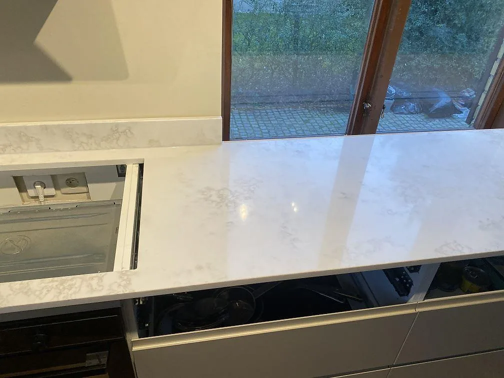 Detalj av polerad Technistone Altamonte, komposit, med hälluttag och lång arbetsyta framför fönster i Landskrona.
