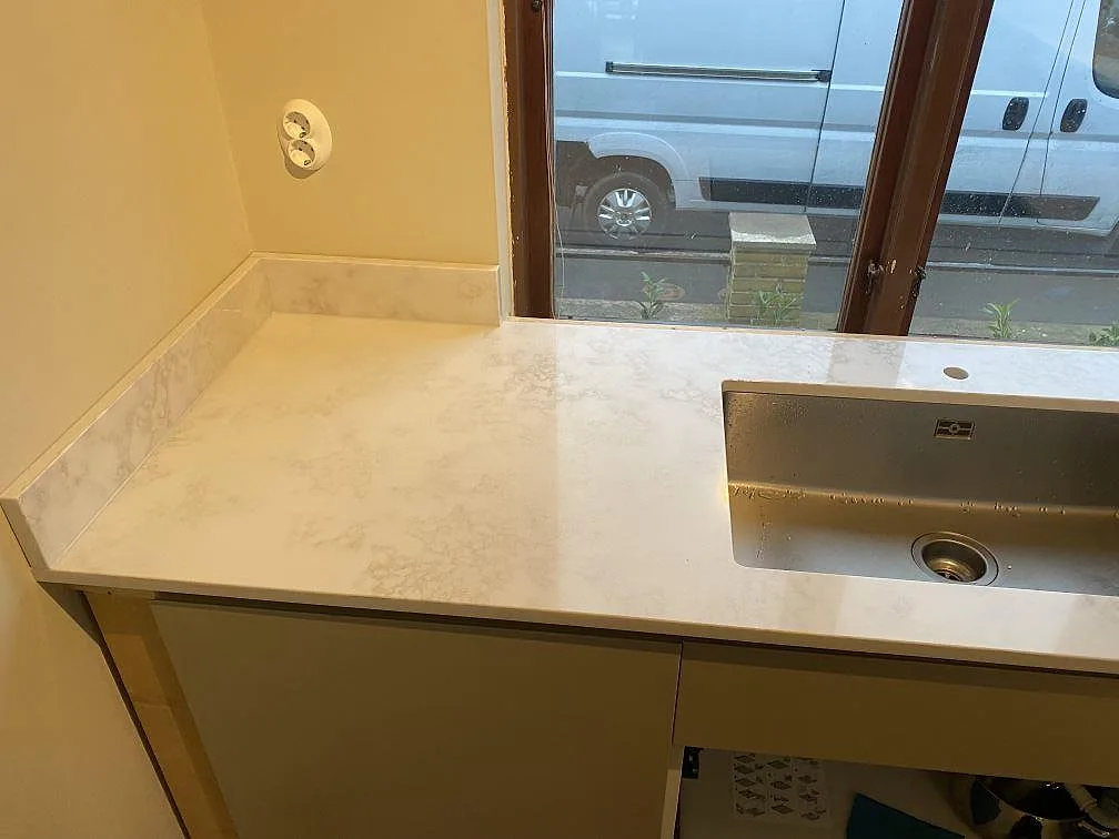 Köksbänkskiva i polerad Technistone Altamonte, komposit, med rostfri underlimmad diskho och stänkkant vid fönster i Landskrona.