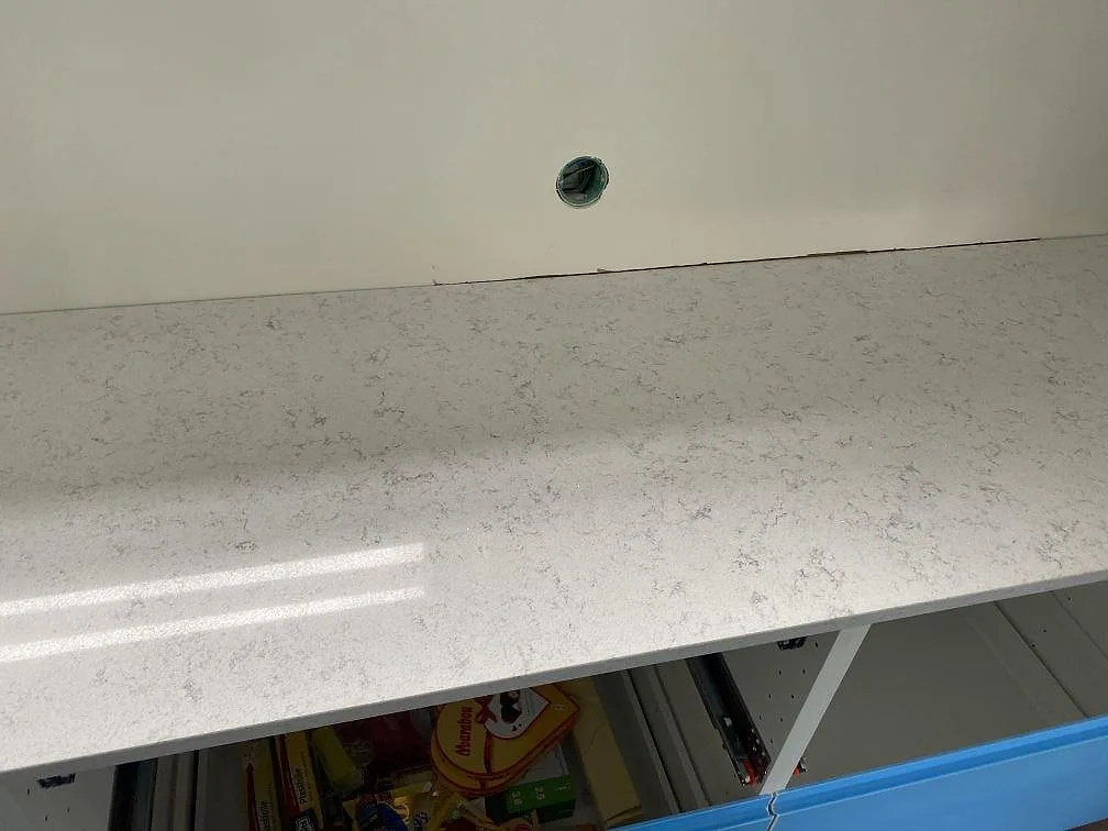 Polerad köksbänkskiva i vit Technistone Brilliant Arabesco med grå ådring monterad ovanpå köksstommar i ett kök i Vallberga.