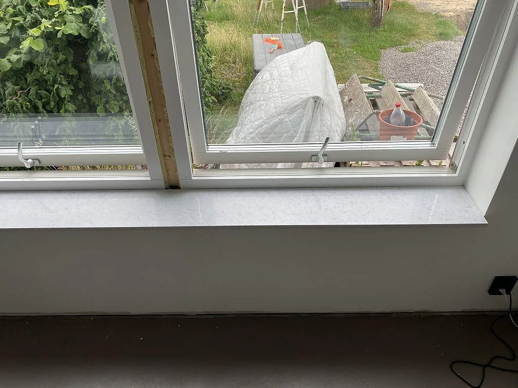Fönsterbänk i vit Technistone Brilliant Arabesco med grå ådring vid ett köksfönster i Vallberga.