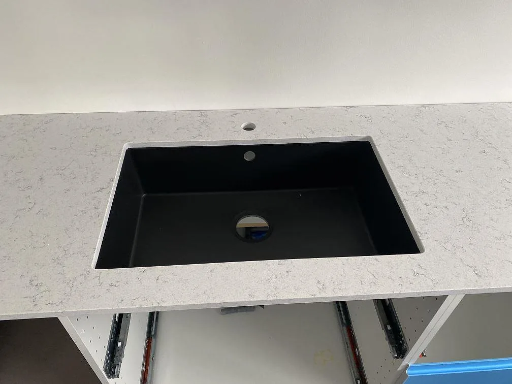 Närbild på svart underlimmad kompositdiskho i en vit köksbänkskiva i Technistone Brilliant Arabesco med grå ådring i Vallberga.