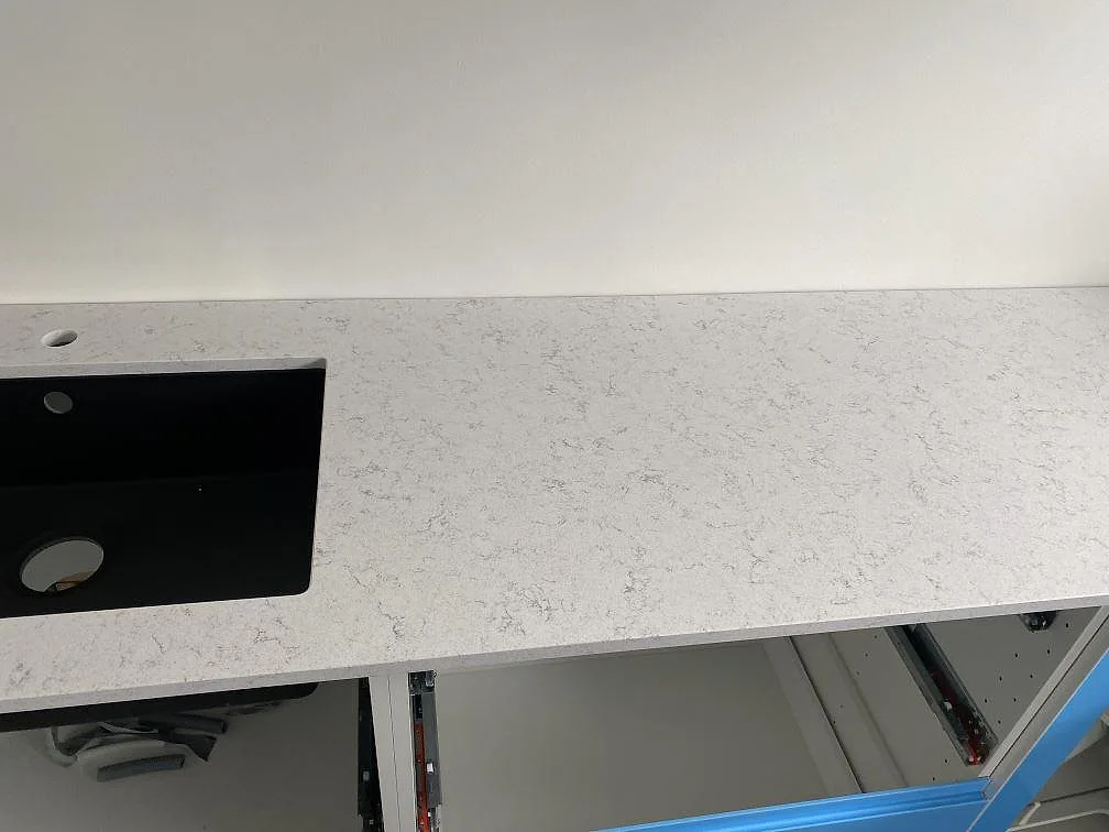 Polerad köksbänkskiva i Technistone Brilliant Arabesco med svart underlimmad kompositdiskho och separat borrat blandarhål i ett kök i Vallberga.