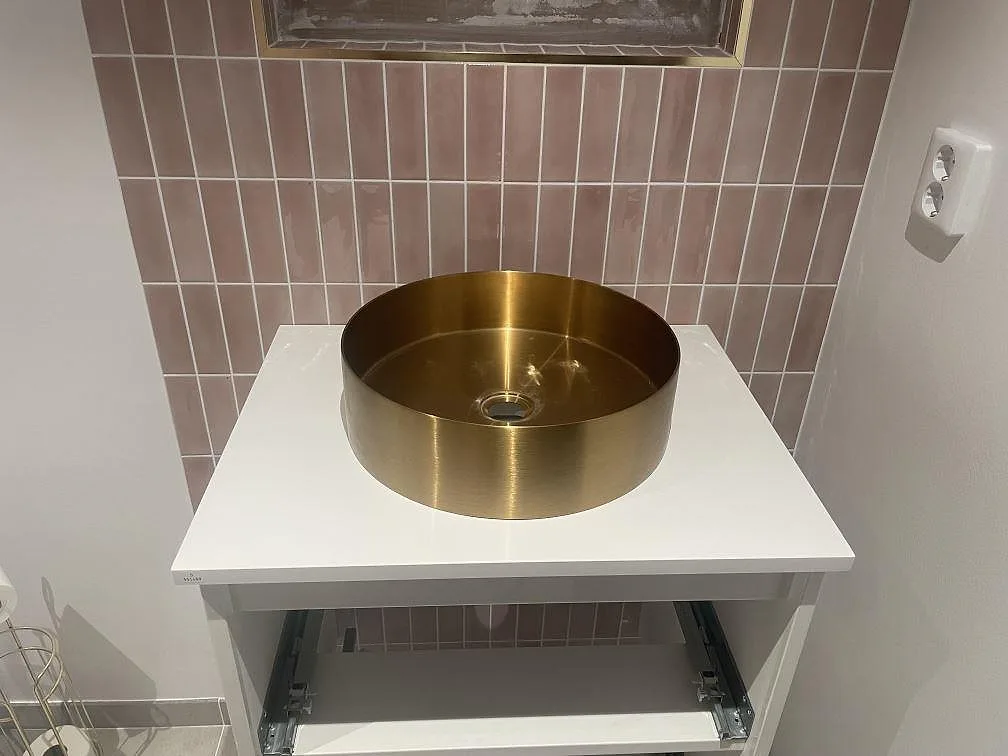 Badrumsbänkskiva i vit Technistone Crystal Absolute White, polerad komposit, med rund guldfärgad tvättställsskål och rosa kakel i Enköping.