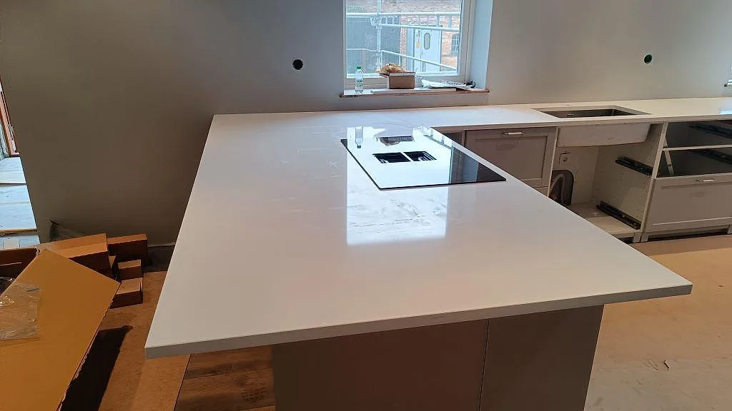 Stor köksö i polerad Technistone Crystal Absolute White med svart häll och anslutande bänk mot diskhon i Fjälkinge.