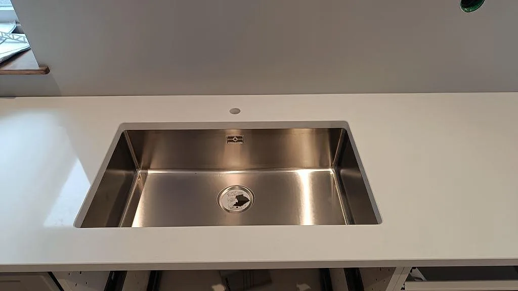 Underlimmad rostfri diskho i polerad Technistone Crystal Absolute White, vit kompositbänkskiva, i ett kök i Fjälkinge.