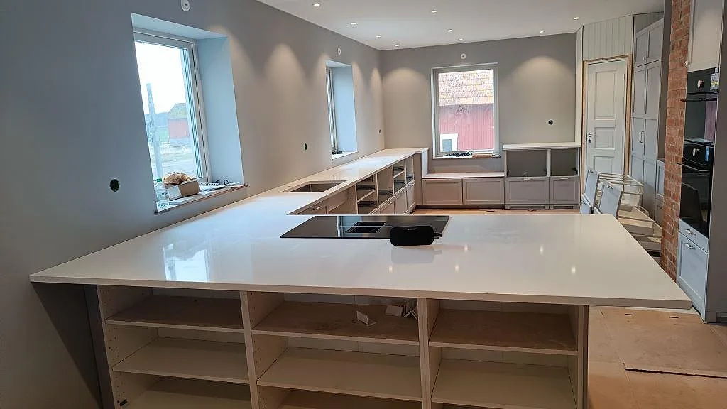 Köksbänkskiva i vit Technistone Crystal Absolute White, polerad komposit, med stor köksö och svart häll i ett kök i Fjälkinge.