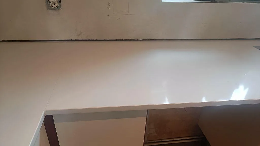 Lång köksbänkskiva i polerad Technistone Crystal Absolute White längs vägg med öppna stommar i Glumslöv.