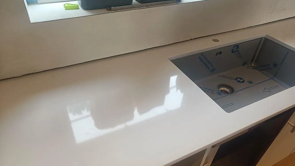 Köksbänkskiva i Technistone Crystal Absolute White, polerad vit komposit, med underlimmad rostfri diskho vid fönster i Glumslöv.